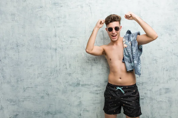 Özel bir günü kutlayan mayo giyen genç beyaz adam, atlıyor ve enerjiyle kollarını kaldırıyor.