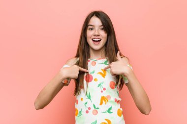 Girl wearing a summer clothes against a red wall surprised pointing with finger, smiling broadly. clipart