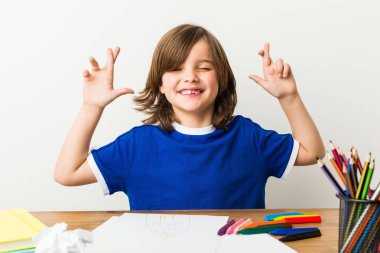 Küçük çocuk resim ve şans için parmaklarını geçiş masasında ödevleri yapıyor