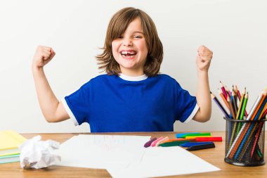 Küçük çocuk resim ve onun masasında kaygısız ve heyecanlı tezahürat ev ödevi yapıyor. Zafer kavramı.