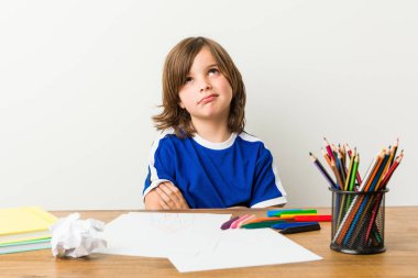 Küçük çocuk resim ve alaycı ifade ile kamera bakarak mutsuz masasında ödevleri yapıyor.