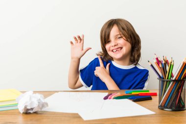 Little boy painting and doing homeworks on his desk pointing with forefingers to a copy space, expressing excitement and desire. clipart