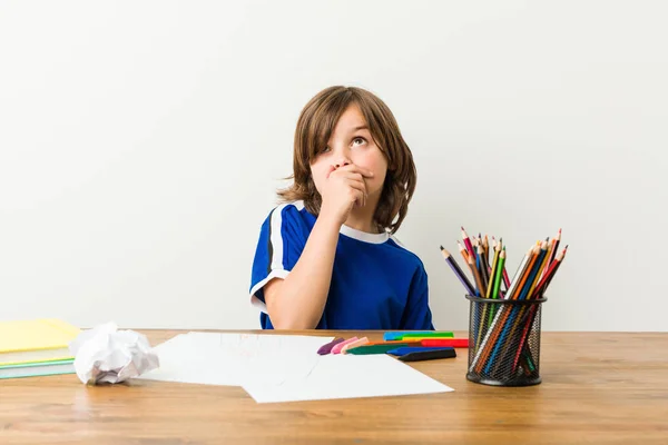 小さな男の子が絵を描き 手で口を覆うコピースペースを見て思慮深く彼の机の上で宿題をする — ストック写真