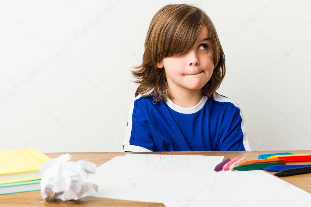 Little boy painting and doing homeworks on his desk confused, feels doubtful and unsure.