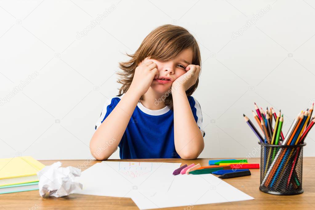 Little boy painting and doing homeworks on his desk whining and crying disconsolately.