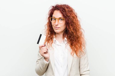 Kredi kartı nı tutan genç beyaz kızıl saçlı kadın mutlu, gülümseyen ve neşeli.