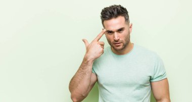 Yeşil bir arka plan aleyhine genç yakışıklı adam işaret parmağı ile bir hayal kırıklığı jest gösteren.