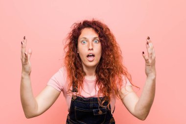 Genç güzel zencefil kızıl saçlı kadın hoş bir sürpriz alan bir kot dungaree giyen, heyecanlı ve ellerini yükselterek.
