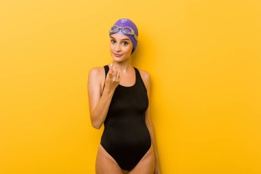 Young swimmer caucasian woman pointing with finger at you as if inviting come closer.