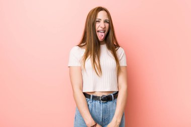 Pembe bir duvara karşı genç kızıl saçlı zencefil kadın komik ve dost dil dışarı yapışmasını.