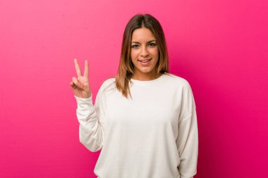 Zafer işareti gösteren ve geniş gülümseyen bir duvara karşı Genç otantik karizmatik gerçek insanlar kadın.