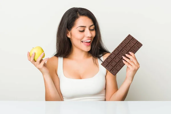 リンゴまたはチョコレートタブレットの間で選択する若いヒスパニック女性 — ストック写真