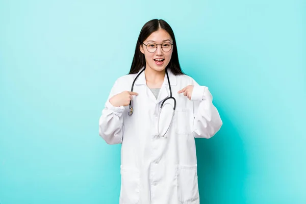 Young chinese doctor woman surprised pointing with finger, smiling broadly.