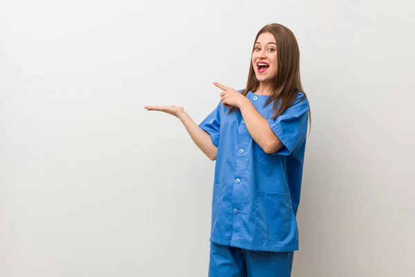 Νεαρή Νοσοκόμα Γυναίκα Εναντίον Ενός Λευκού Τοίχου Ενθουσιασμένα Κρατώντας Ένα — Φωτογραφία Αρχείου