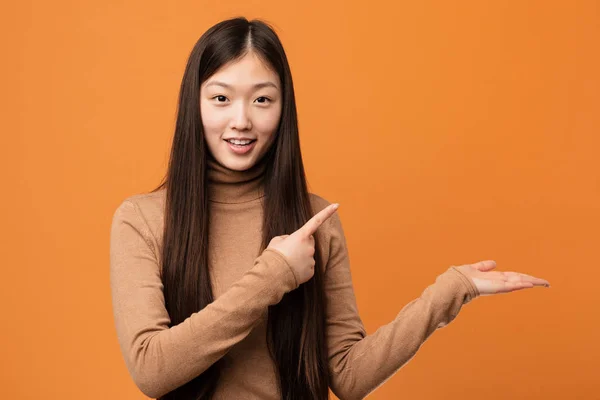 Young pretty chinese woman excited holding a copy space on palm.