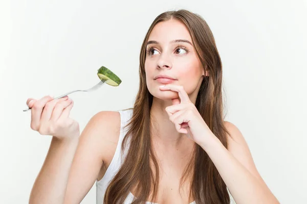 Young Caucasian Woman Eating Cucumber Looking Sideways Doubtful Skeptical Expression — Stockfoto