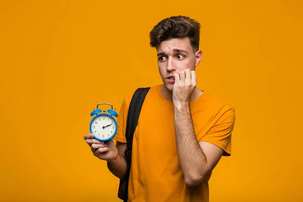 Young Student Man Holding Alarm Clock Crossing Fingers Having Luck — Stock Photo, Image