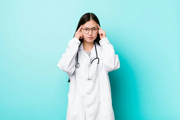 Young chinese doctor woman focused on a task, keeping forefingers pointing head.