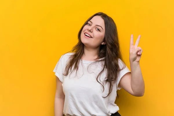 Young curvy plus size woman joyful and carefree showing a peace symbol with fingers.