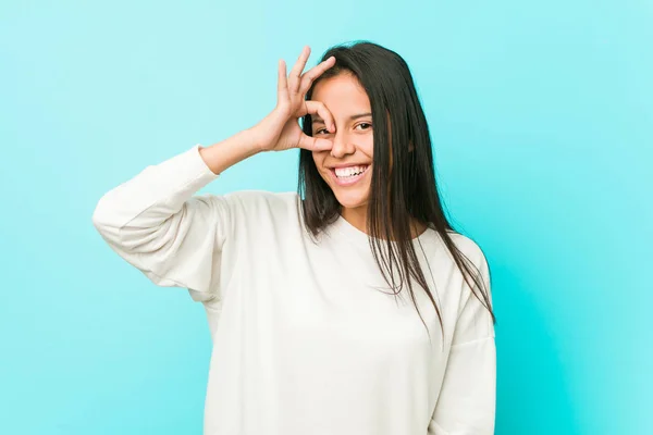 Young pretty hispanic woman excited keeping ok gesture on eye.