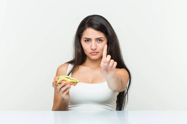 Young Hispanic Woman Holding Avocado Toast Showing Number One Finger — Stock Photo, Image