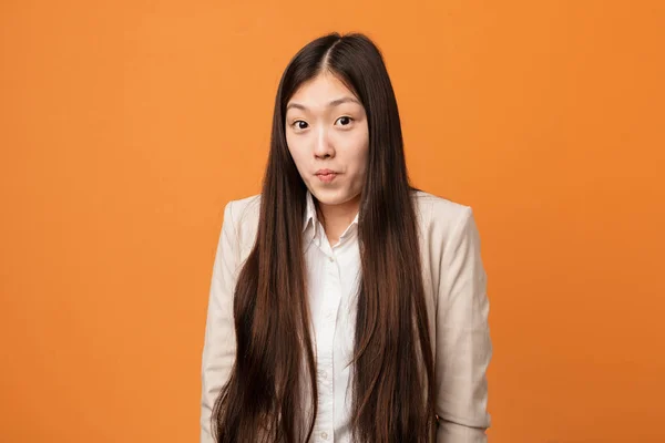 Young business chinese woman shrugs shoulders and open eyes confused.