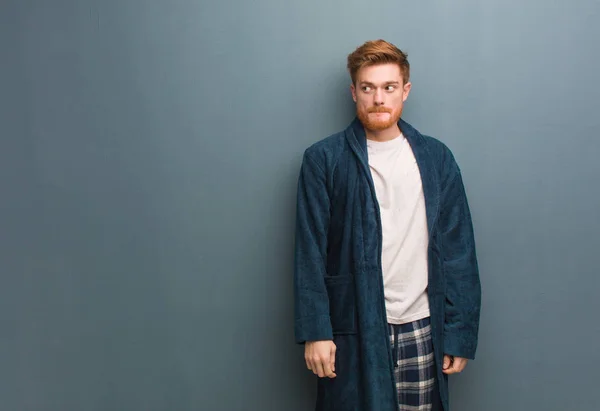 Young redhead man in pajama thinking about an idea