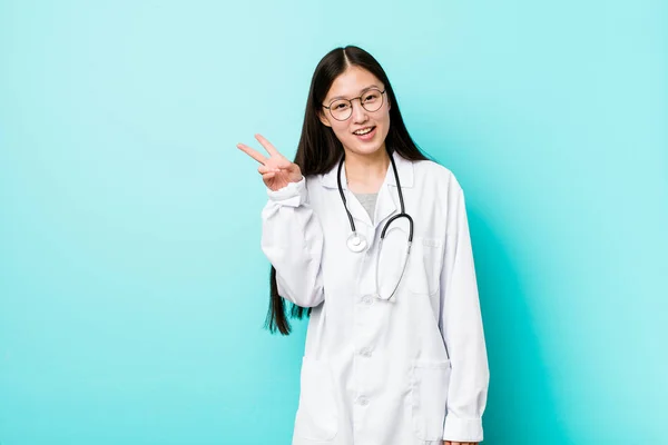 Young chinese doctor woman joyful and carefree showing a peace symbol with fingers.