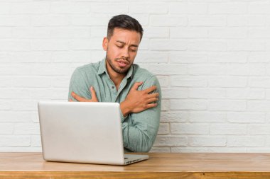 Genç filipinli adam onun laptop hugs ile çalışan oturan, kaygısız ve mutlu gülümseyen.