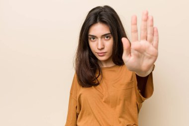 Genç esmer kadın bir bej arka plan karşı uzanmış el dur işareti gösteren ayakta, sizi engelleyen.