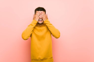 Genç İspanyol adam elleri ile gözleri kaplar, geniş bir sürpriz bekliyor gülümsüyor.