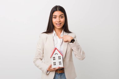 Young arab woman holding a house icon surprised pointing at himself, smiling broadly. clipart