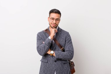 Beyaz bir duvara karşı genç iş filipino adam mutlu ve kendinden emin gülümseyen, el ile çene dokunmadan.