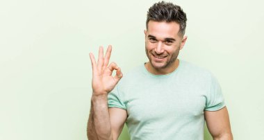 Yeşil bir arka plan neşeli ve kendinden emin ok jest gösteren karşı Genç yakışıklı adam.