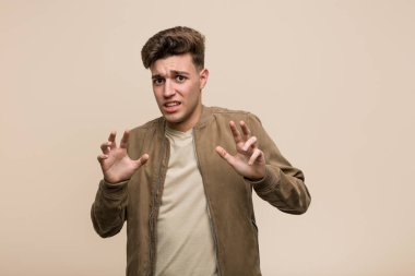 Kahverengi ceket giyen genç beyaz adam iğrenme jesti gösteren birini reddediyor.