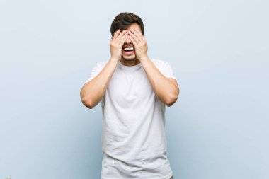 Beyaz bir tişört giyen genç beyaz adam elleri ile gözleri kaplıyor, gülümsüyor geniş bir sürpriz bekliyor.