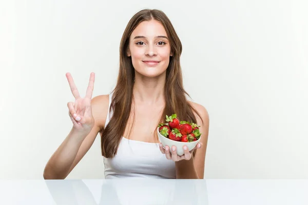 Young Caucasian Woman Holding Strawberries Bowl Showing Number Two Fingers — Stockfoto