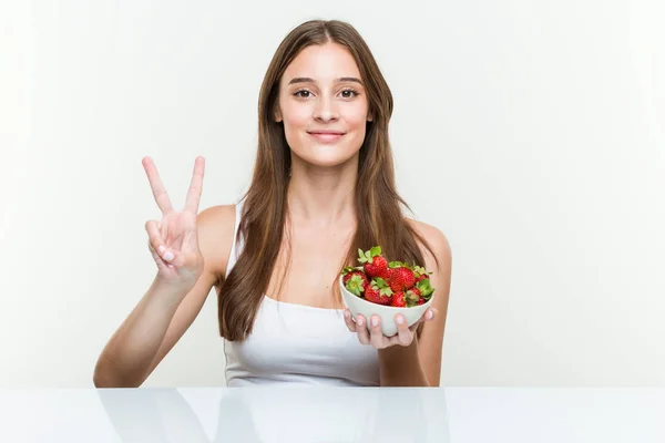 Young Caucasian Woman Holding Strawberries Bowl Showing Number Two Fingers — Zdjęcie stockowe