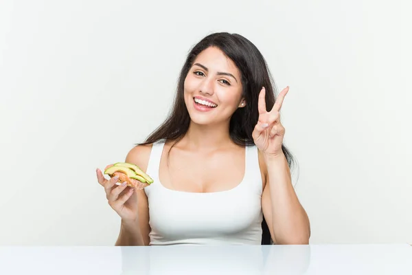 Young Hispanic Woman Holding Avocado Toast Showing Victory Sign Smiling — Stock Photo, Image