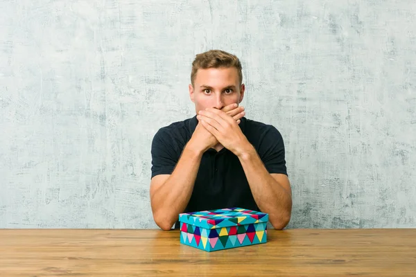 Young Caucasian Man Holding Gift Box Table Shocked Covering Mouth — Stock Photo, Image