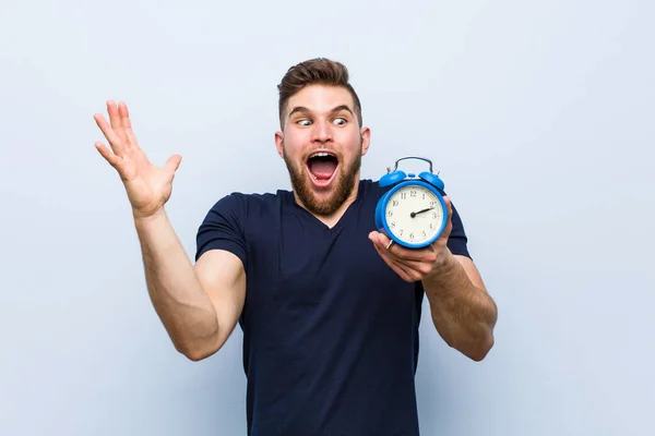 Young Caucasian Man Holding Alarm Clock Celebrating Victory Success — Stock Photo, Image