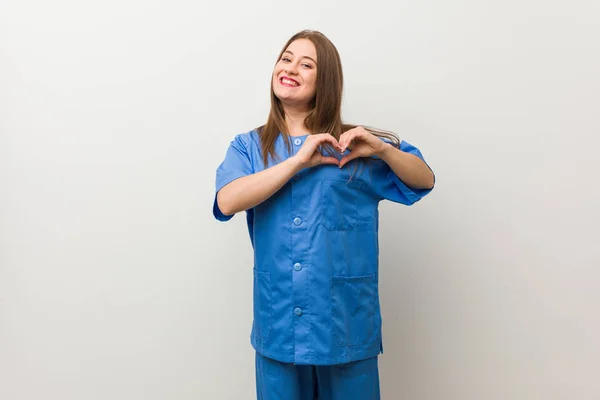 Jonge Verpleegster Vrouw Tegen Een Witte Muur Glimlachend Toont Een — Stockfoto