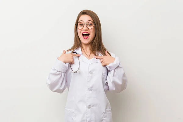 Jonge Dokter Vrouw Tegen Een Witte Muur Verrast Wijzend Met — Stockfoto