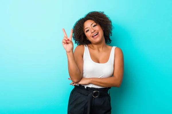 Young african american woman joyful and carefree showing a peace symbol with fingers.