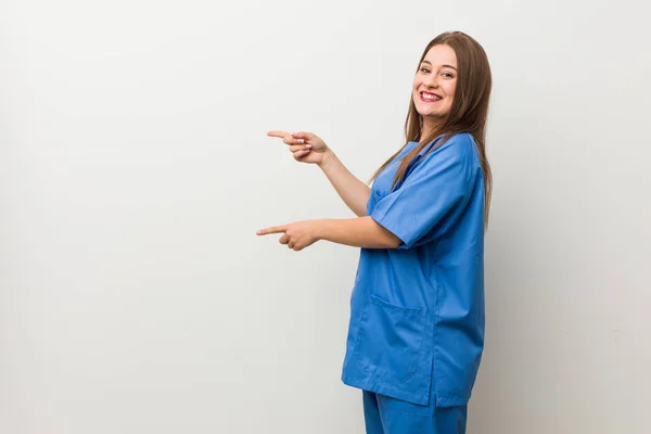 Νεαρή Νοσοκόμα Γυναίκα Ένα Λευκό Τοίχο Ενθουσιασμένος Δείχνοντας Τους Δείκτη — Φωτογραφία Αρχείου