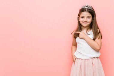 Bir prenses giyen küçük kız gülümseyen ve bir kenara işaret, boş alanda bir şey gösteren bakmak.