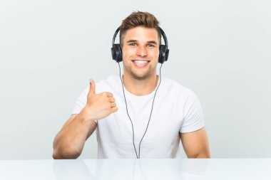 Kulaklıkla müzik dinleyen genç adam gülümseyerek ve başparmağını yukarı kaldırarak