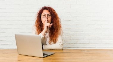 Genç kızıl saçlı kıvırcık kadın dizüstü bilgisayar ile çalışan bir sır tutmak veya sessizlik isteyen.