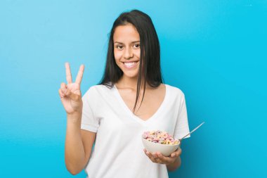 Genç İspanyol kadın parmakları ile iki numara gösteren bir şeker tahıl kase tutan.