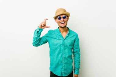 Genç İspanyol adam bir yaz giysileri giyen ön parmakları ile küçük bir şey tutan, gülümseyen ve kendinden emin.